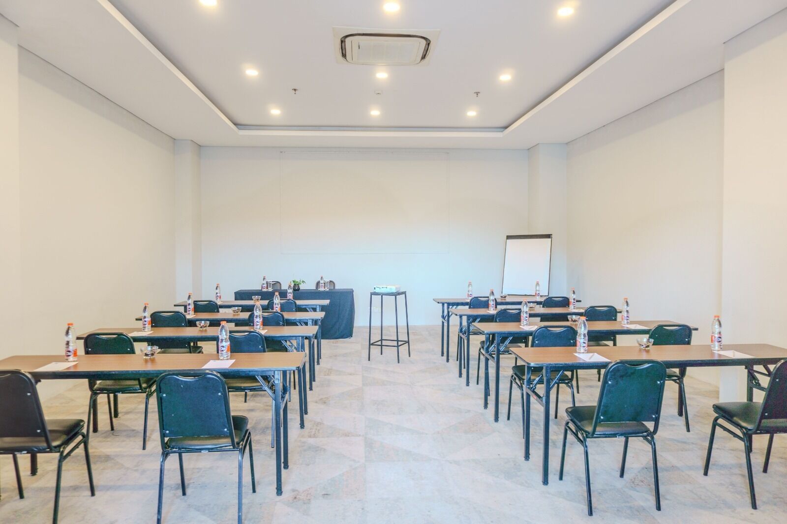 Une salle de conférence dotée de plusieurs tables et chaises, ainsi que de bouteilles d’eau et d’un tableau blanc.