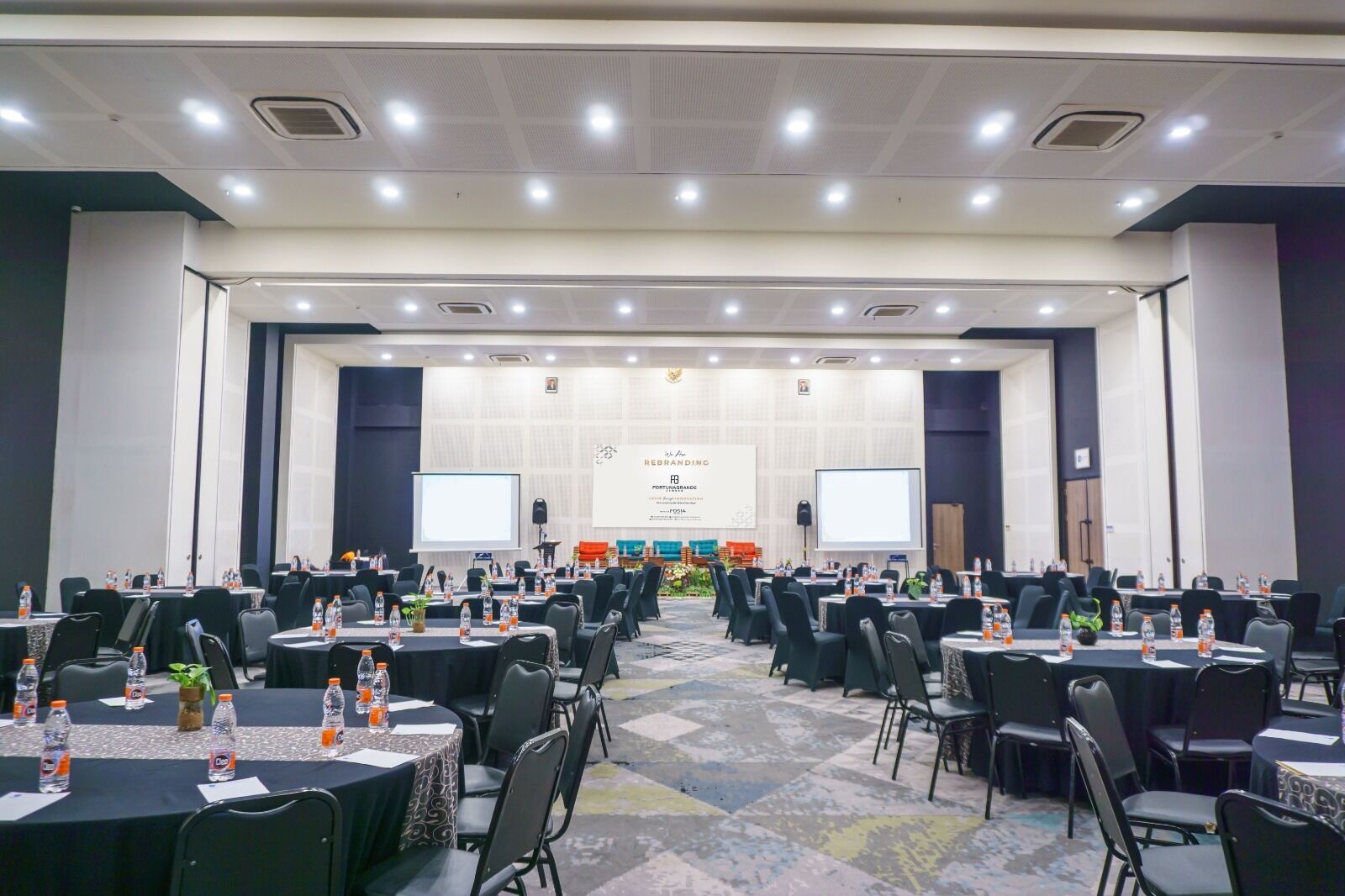 A conference room with multiple tables and chairs, equipped with water bottles and projectors.