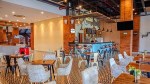 Um restaurante com área de bar, várias mesas e cadeiras, e um chão estampado.
