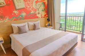 A large bed with a headboard, a bedside table, a nightstand, and a view of a balcony with a railing. - Hotel FortunaGrande Jember (Jember)