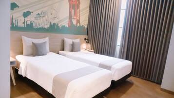 Habitación de hotel con dos camas, un mural de la ciudad, una mesita de noche, una lámpara y un ventanal con cortinas.