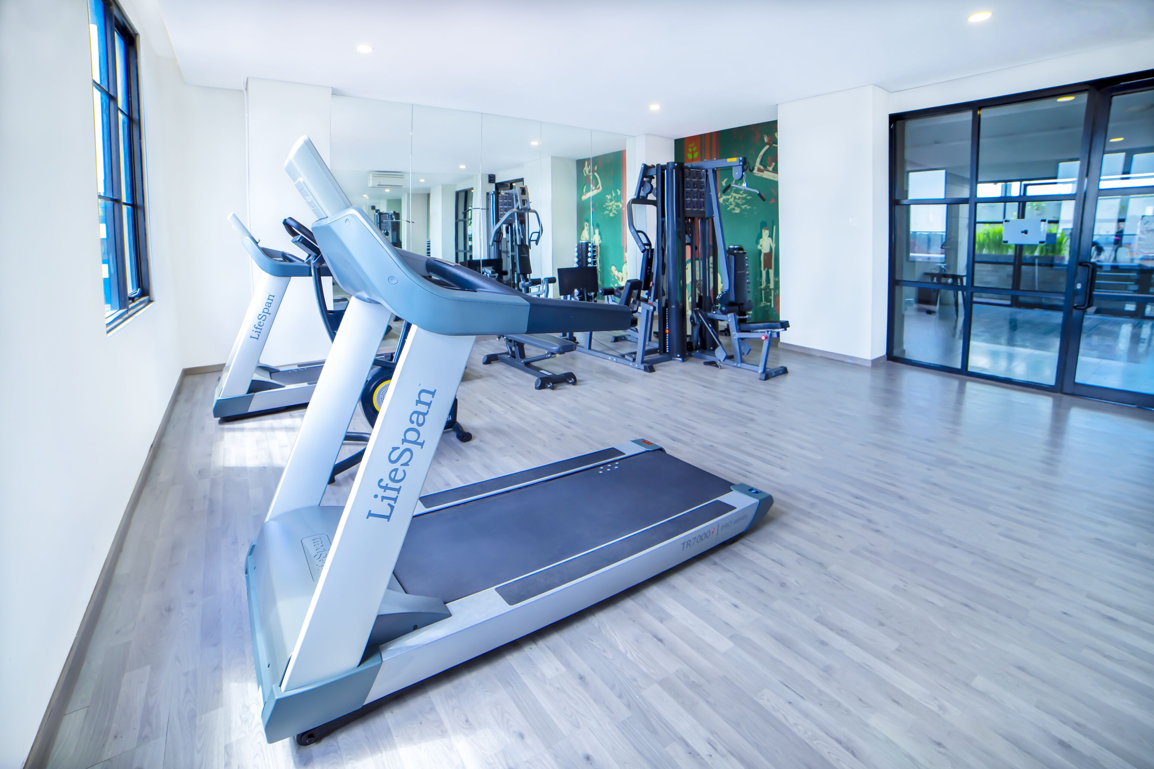 Un gimnasio con cintas de correr, máquinas de pesas y un muro de espejos.