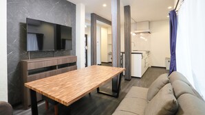 A modern living room with a wooden dining table, a sofa, and a TV mounted on a marble wall. - Villa Ikebukuro Altair (Tokyo)