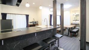 A modern kitchen with a marble countertop, a sink, a microwave, and a dining area with a table and chairs. - Villa Ikebukuro Altair (Tokyo)
