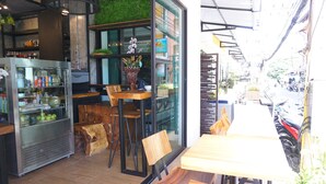An indoor café with wooden furniture, a refrigerated display case, and a view of the street outside. - Buasri by Ohm (Patong)