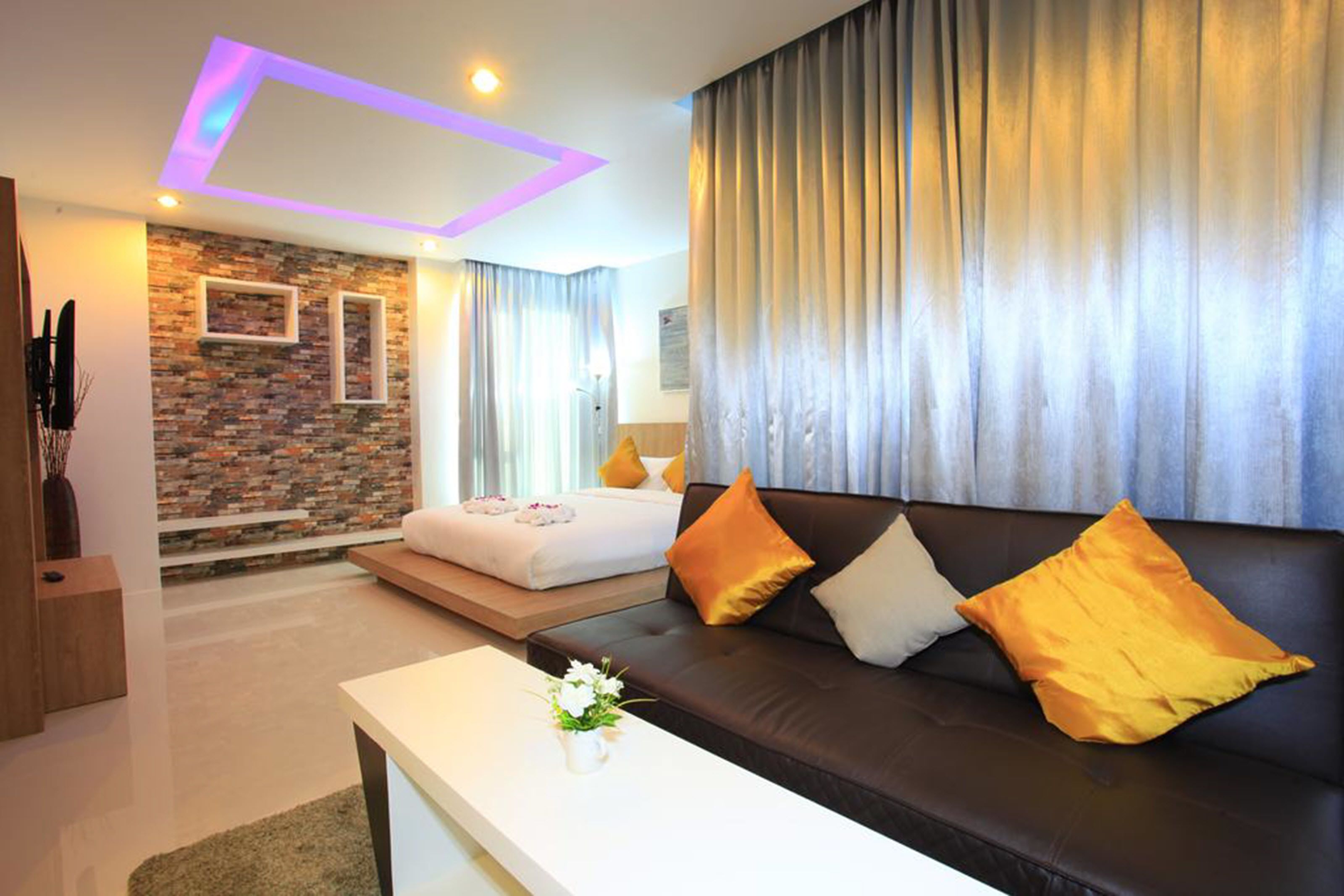 Une chambre d’hôtel moderne avec un mur d’accent en briques, un canapé en cuir noir et un lit blanc.