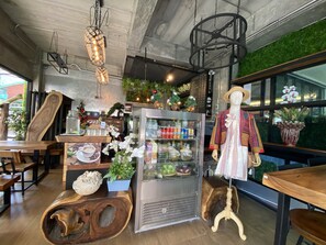 A café interior with a wooden counter, a refrigerated display case, and a mannequin dressed in traditional attire. - Buasri by Ohm (Patong)