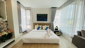 A modern hotel room with a large bed, a wooden platform, a nightstand, a sofa, and a painting on the wall. - Buasri by Ohm (Patong)