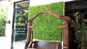 A wooden bench with a rustic design, positioned in front of a shop with a green wall and a glass door displaying contact information. - Buasri by Ohm (Patong)
