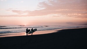 A beach scene with two people walking along the shore, each carrying a surfboard. - Sleep Box Patong - Hostel (Patong)