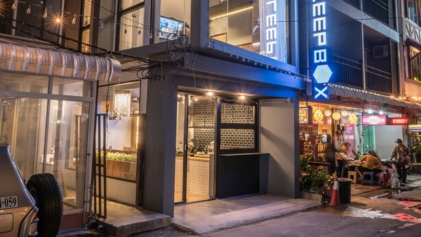 A modern hotel with a prominent 'SLEEPB' sign, large windows, and a visible outdoor seating area. - Sleep Box Patong - Hostel (Patong)