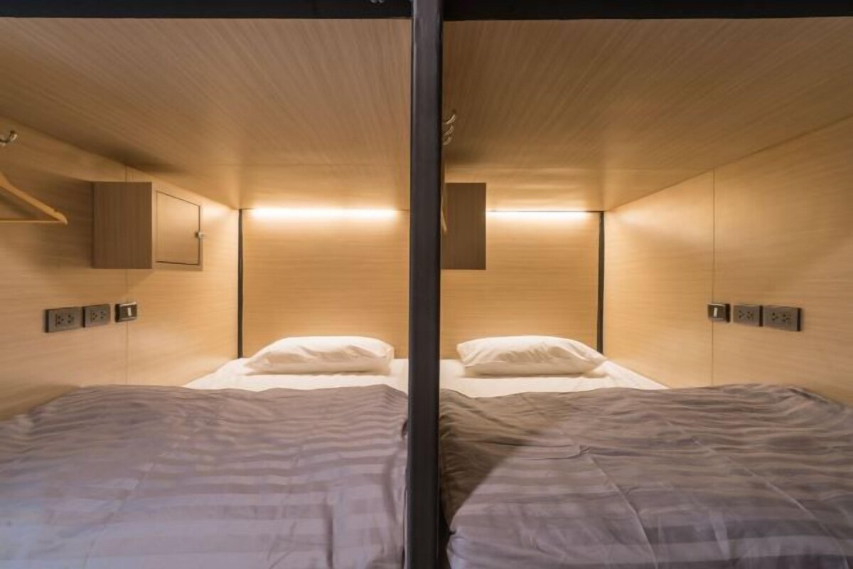 A modern hotel room with two beds, wooden walls, and built-in lighting.