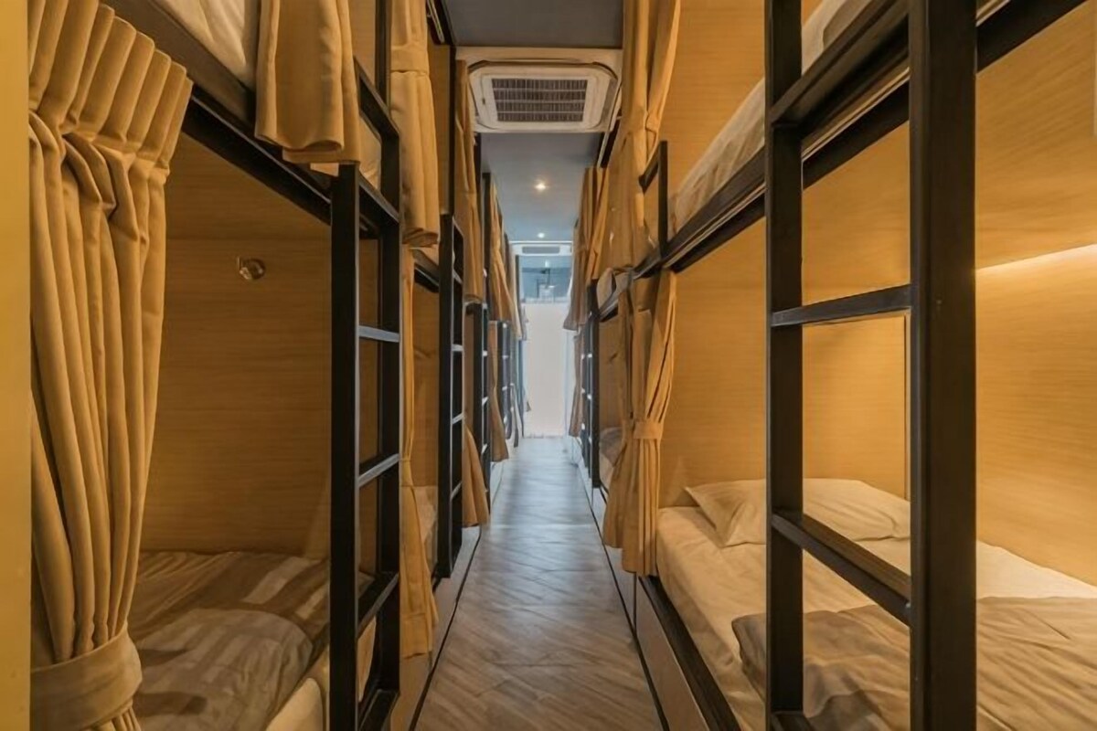 Un pasillo estrecho con literas a ambos lados, un equipo de aire acondicionado y cortinas.
