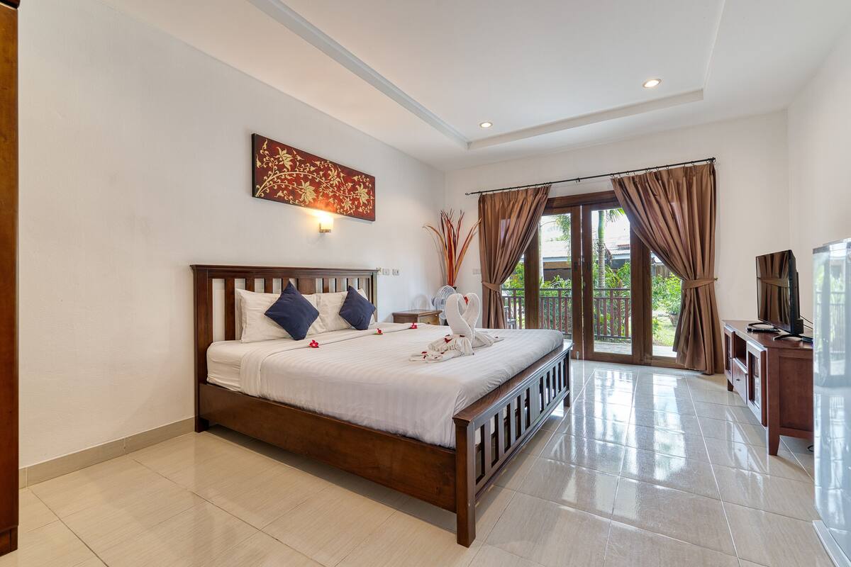 A spacious bedroom with a large bed, a wooden headboard, a nightstand, and a wall-mounted light fixture.