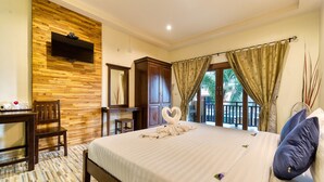 A hotel room with a large bed, a TV mounted on a wooden wall, a desk with a chair, and a view of the outside through a window with curtains. - The Bulin Residence (Koh Samui)