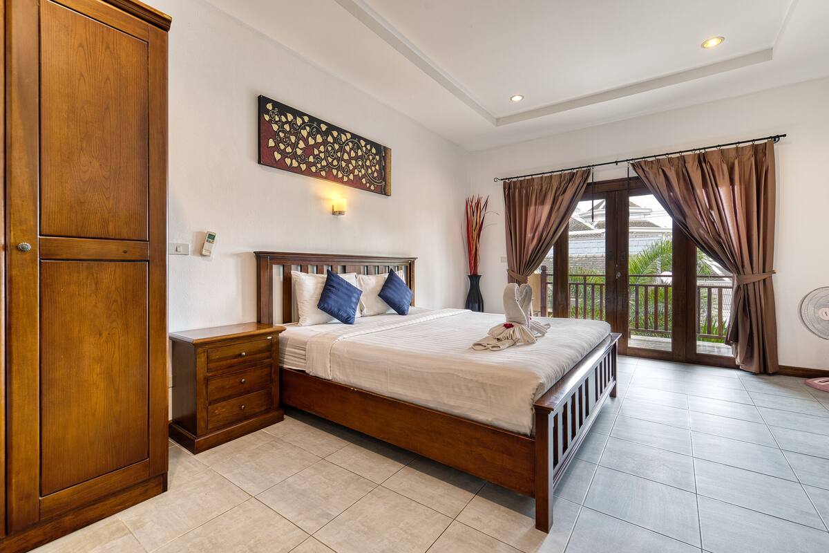 A bedroom with a wooden bed, a nightstand, a wardrobe, and a large window with curtains.