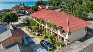 A multi-story building with a red roof, surrounded by greenery and a clear view of the sea. - The Bulin Residence (Koh Samui)