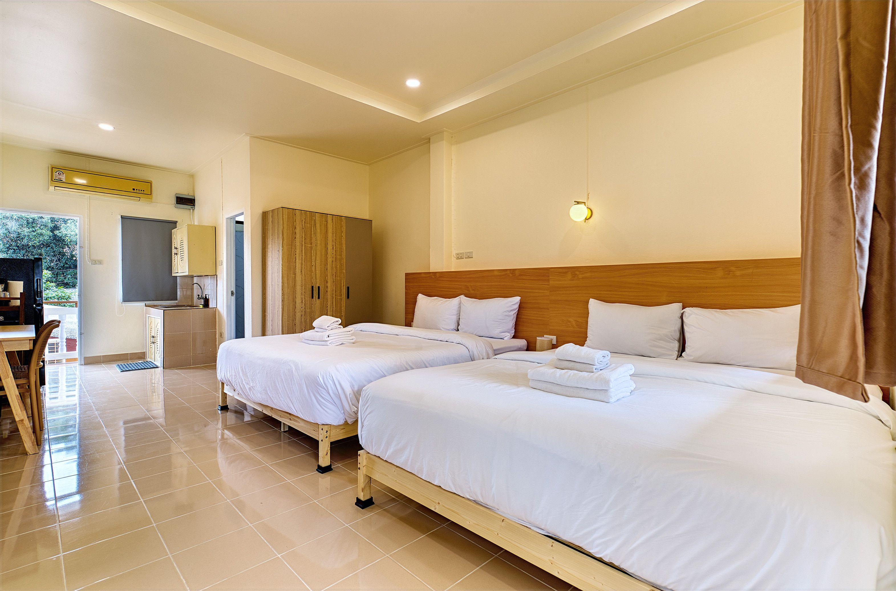 Habitación de hotel con dos camas, cabecera de madera, un escritorio pequeño y una kitchenette.