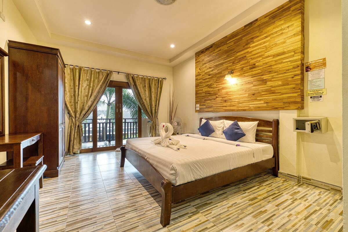 A bedroom with a wooden bed, a desk, and a balcony with curtains.
