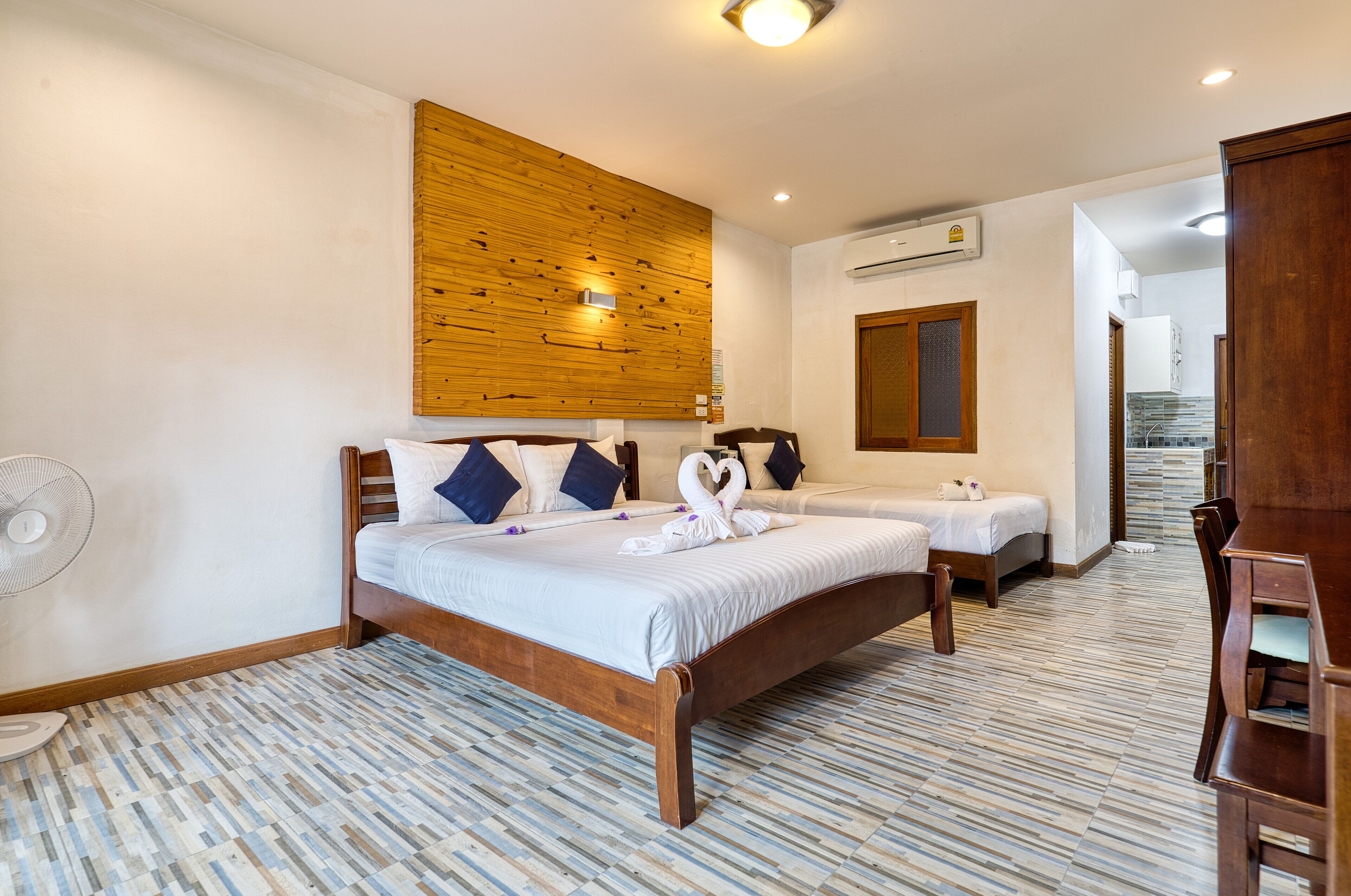 Een hotelkamer met twee bedden, een houten hoofdbord, een ventilator en een vloer met een patroon.