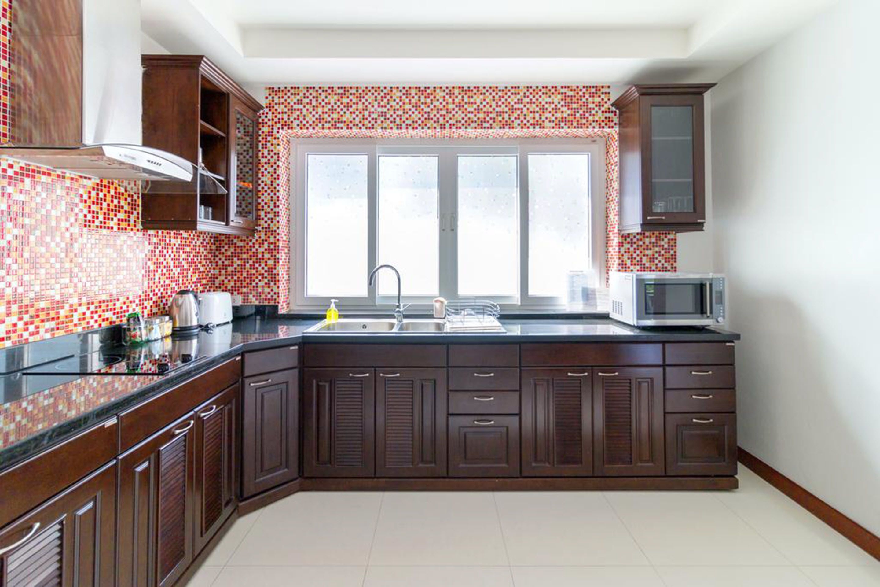 A kitchen with dark wooden cabinets, a black countertop, a window with a view, and a microwave.