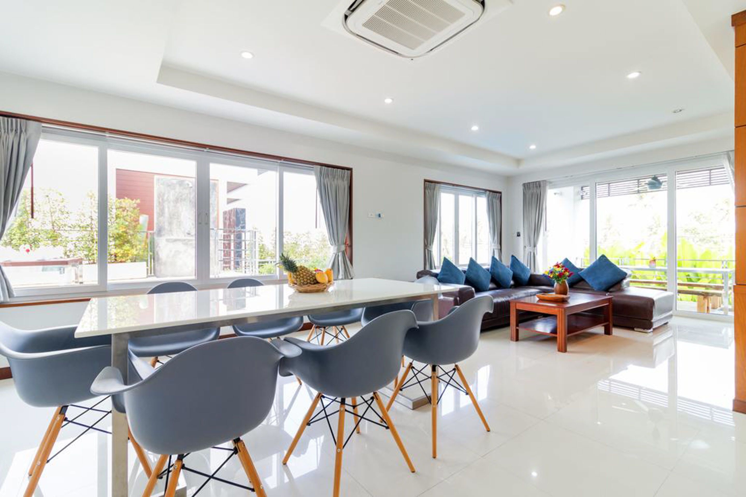 A spacious living room with a large dining table, comfortable seating, and large windows offering a view of the outdoors.