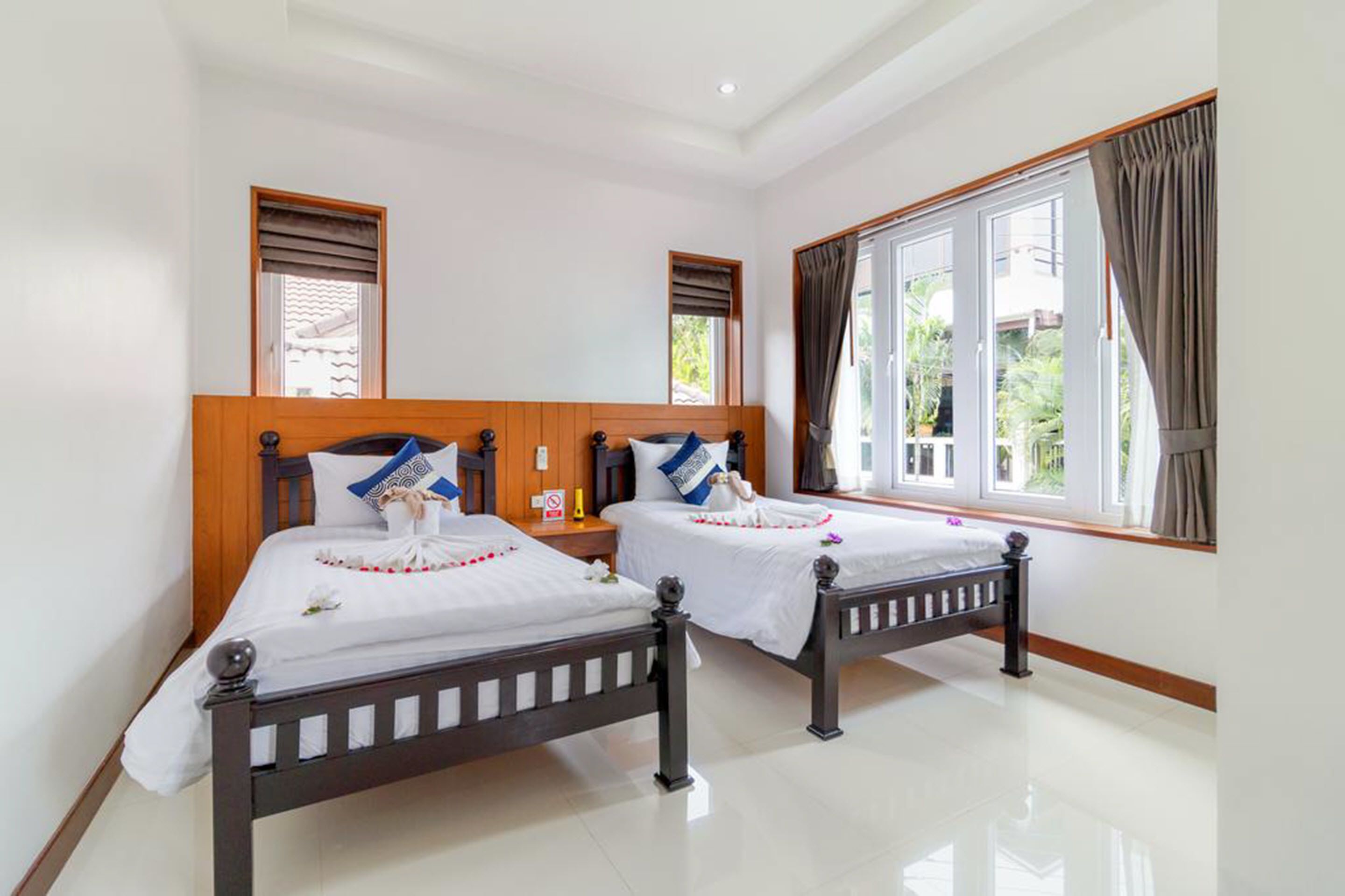 Habitación de hotel con dos camas de madera, ropa de cama blanca y un amplio ventanal con cortinas.