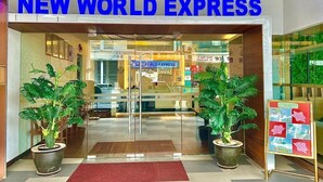 L'ingresso di New World Express, dal design moderno, con porta in vetro, piante in vaso e tappeto rosso.