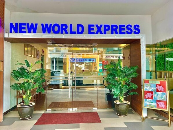 The entrance to New World Express with a modern design, featuring a glass door, potted plants, and a red carpet.