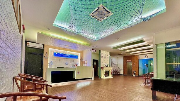 Un'ampia hall con una reception, sedie di legno, un tavolo da biliardo e un soffitto con un motivo geometrico.