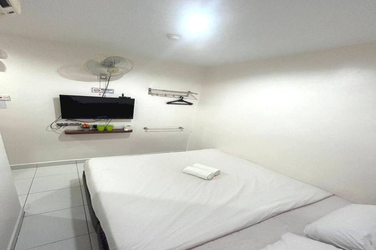 Een hotelkamer met een bed, een aan de muur bevestigde televisie, een ventilator en een handdoek op het bed.