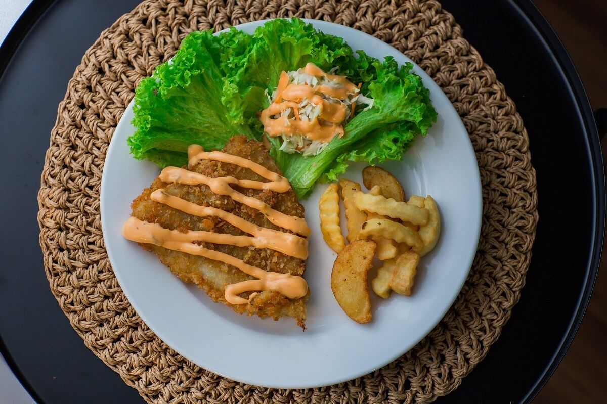 A plate with a breaded cutlet, fries, and a side salad with a creamy sauce.