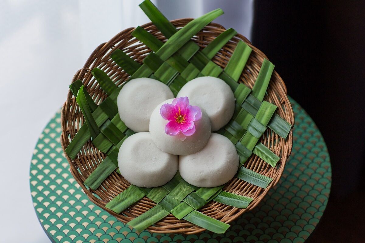 A basket of white round items on a woven mat, surrounded by green leaves.