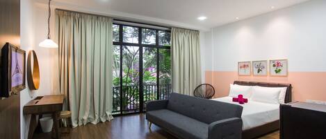A modern hotel room with a large window, a sofa, a bed, a desk, and a television.