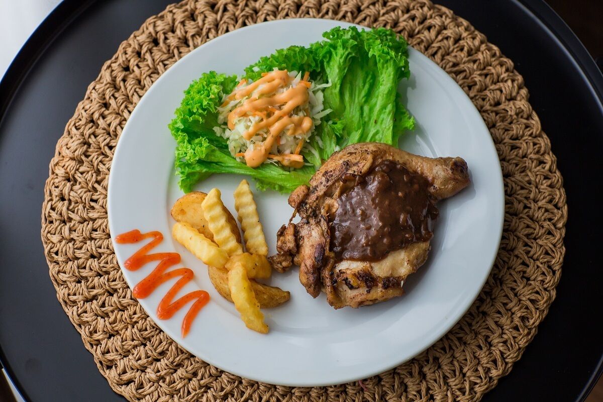 A plate with a grilled chicken leg, French fries, and a side salad with a creamy sauce.