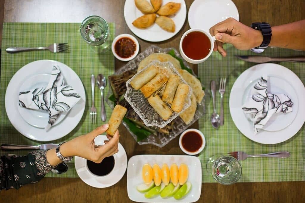 A dining table with plates of food, including spring rolls and a plate of sliced vegetables, and two cups of tea.