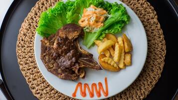 A plate with a meat dish, fries, and a salad on a woven placemat.