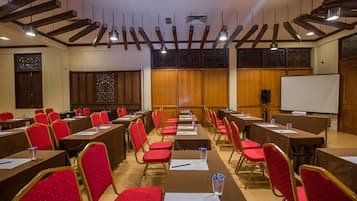 Une salle de conférence avec des rangées de tables et de chaises, un tableau blanc et un projecteur.
