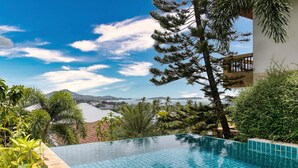A clear view of an infinity pool with a mountain backdrop, surrounded by lush greenery and a modern building.