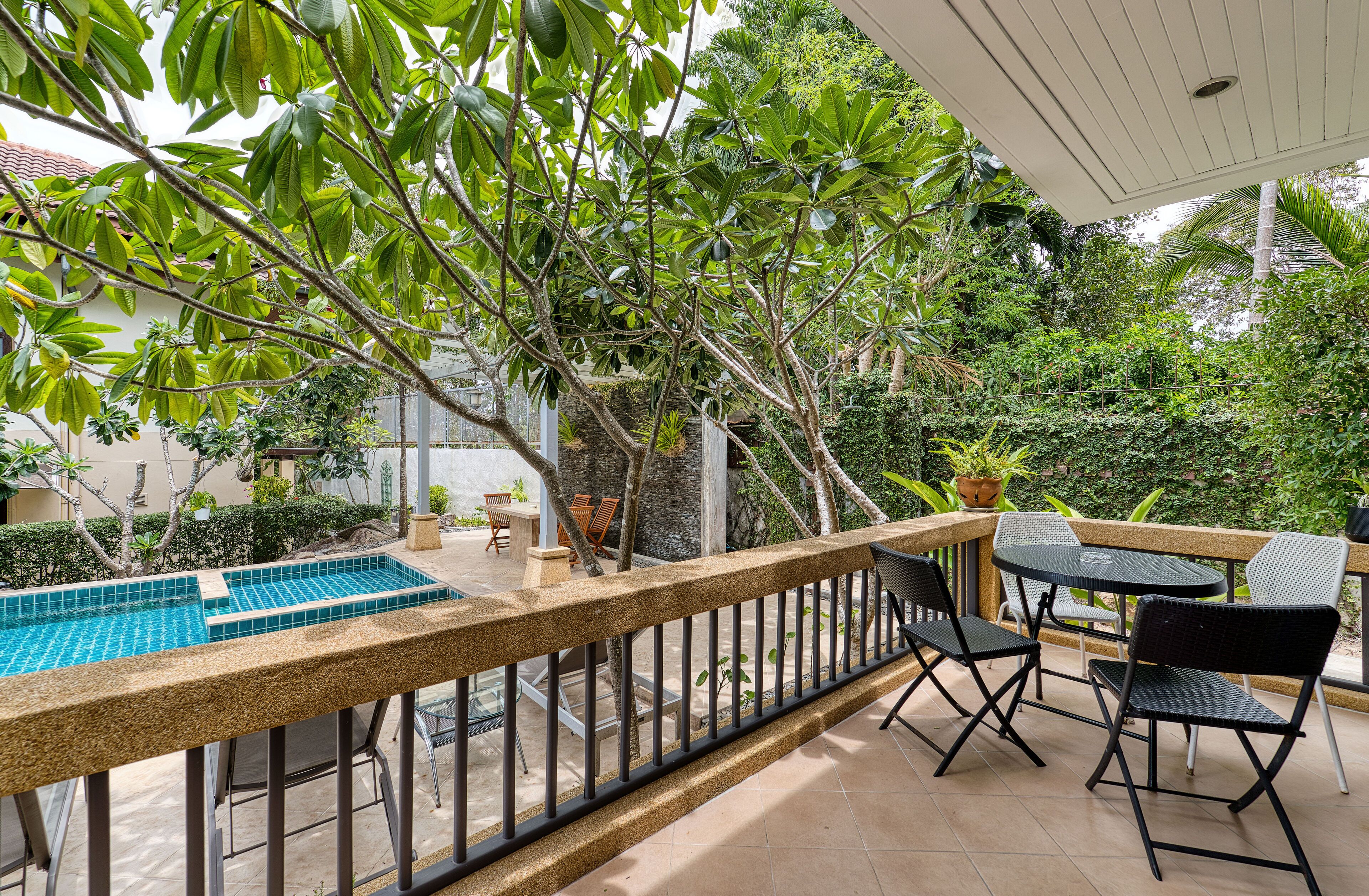 A poolside area with a tiled pool, outdoor furniture, and lush greenery.