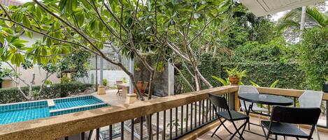 A poolside area with a tiled pool, outdoor furniture, and lush greenery.