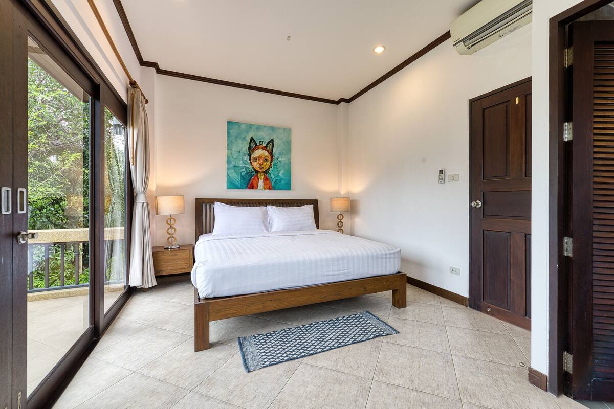 Une chambre avec un grand lit, un tableau accroché au mur et une vue à travers la porte vitrée.