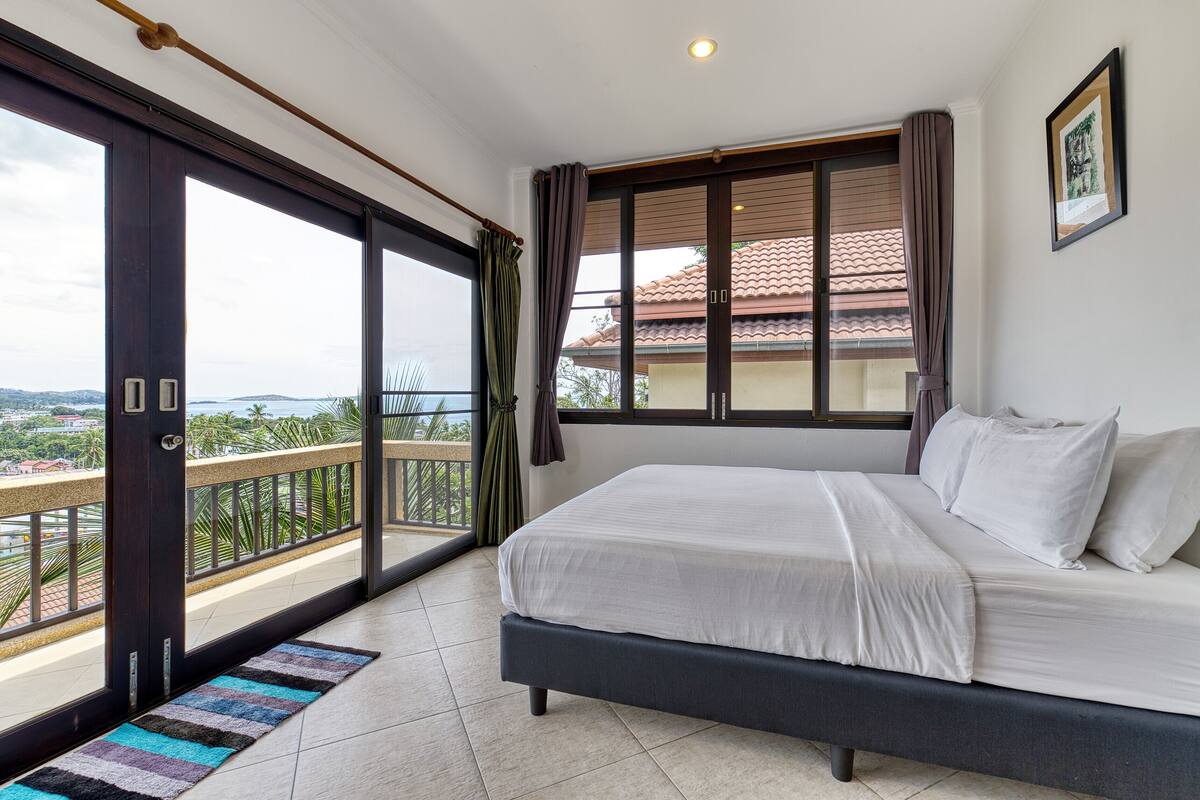 Une chambre à coucher avec un lit, une vue sur la ville et un balcon doté d’une balustrade.