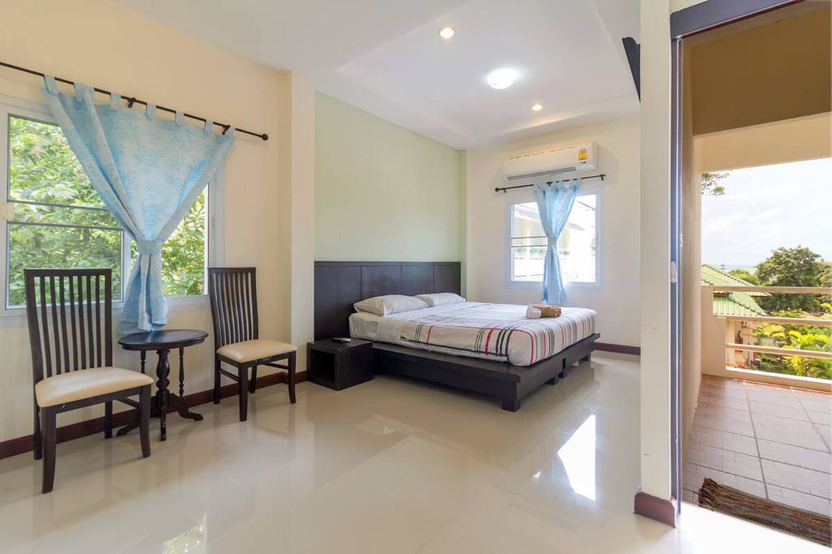 A bedroom with a bed, two chairs, a small table, and a balcony.