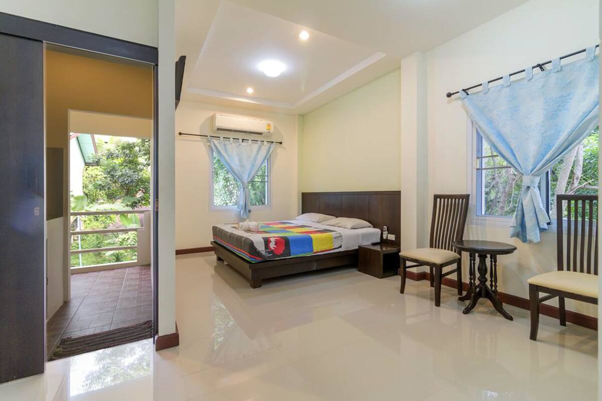 A bedroom with a bed, a chair, a small table, and a window with curtains.
