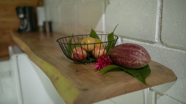 Een keukentafel met een fruitschaal met appels en een rood fruit, een bloem en een groen blad.