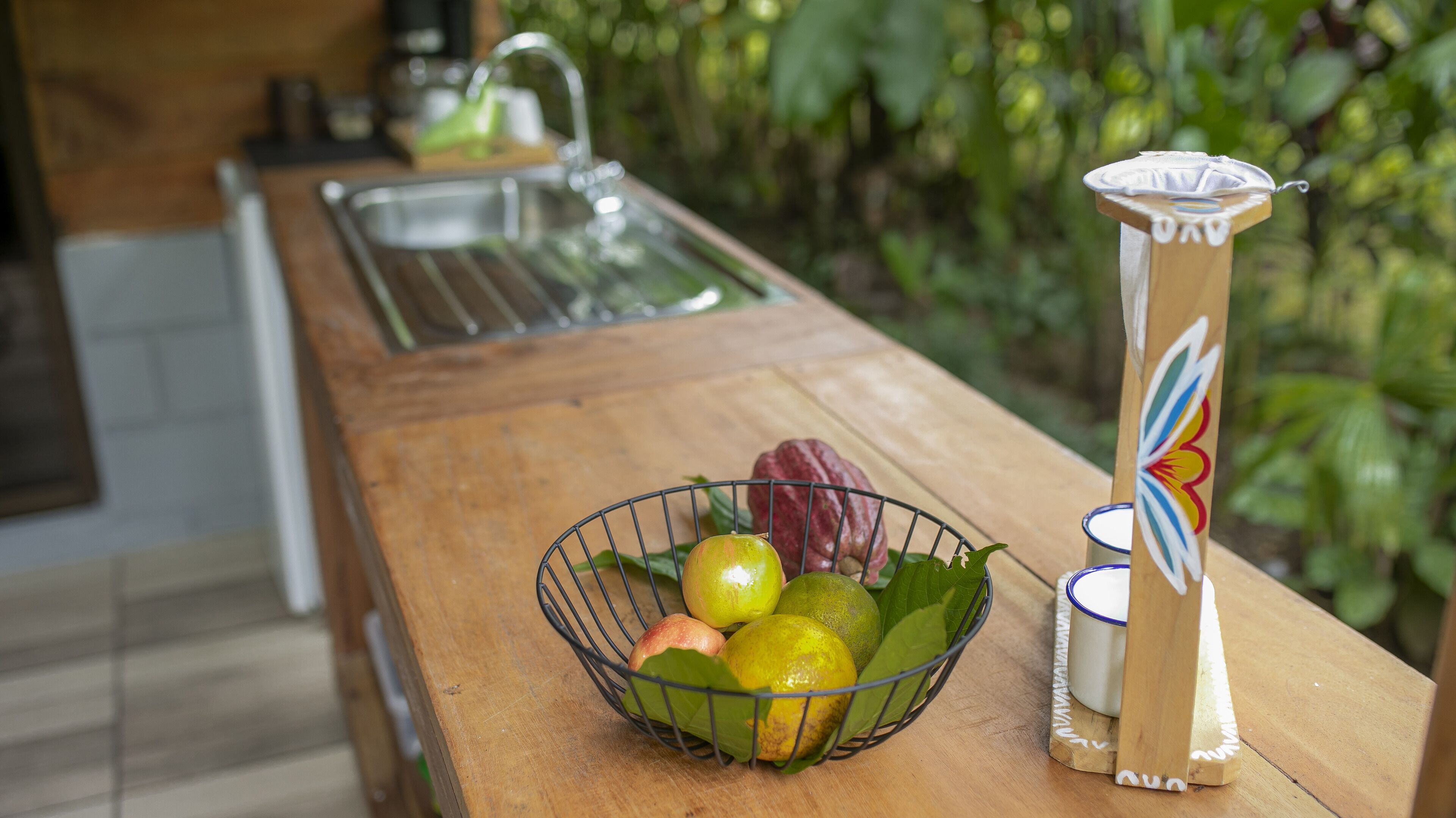 Una encimera de cocina con un frutero que contiene manzanas y limones, un lavamanos y un jarrón decorativo.