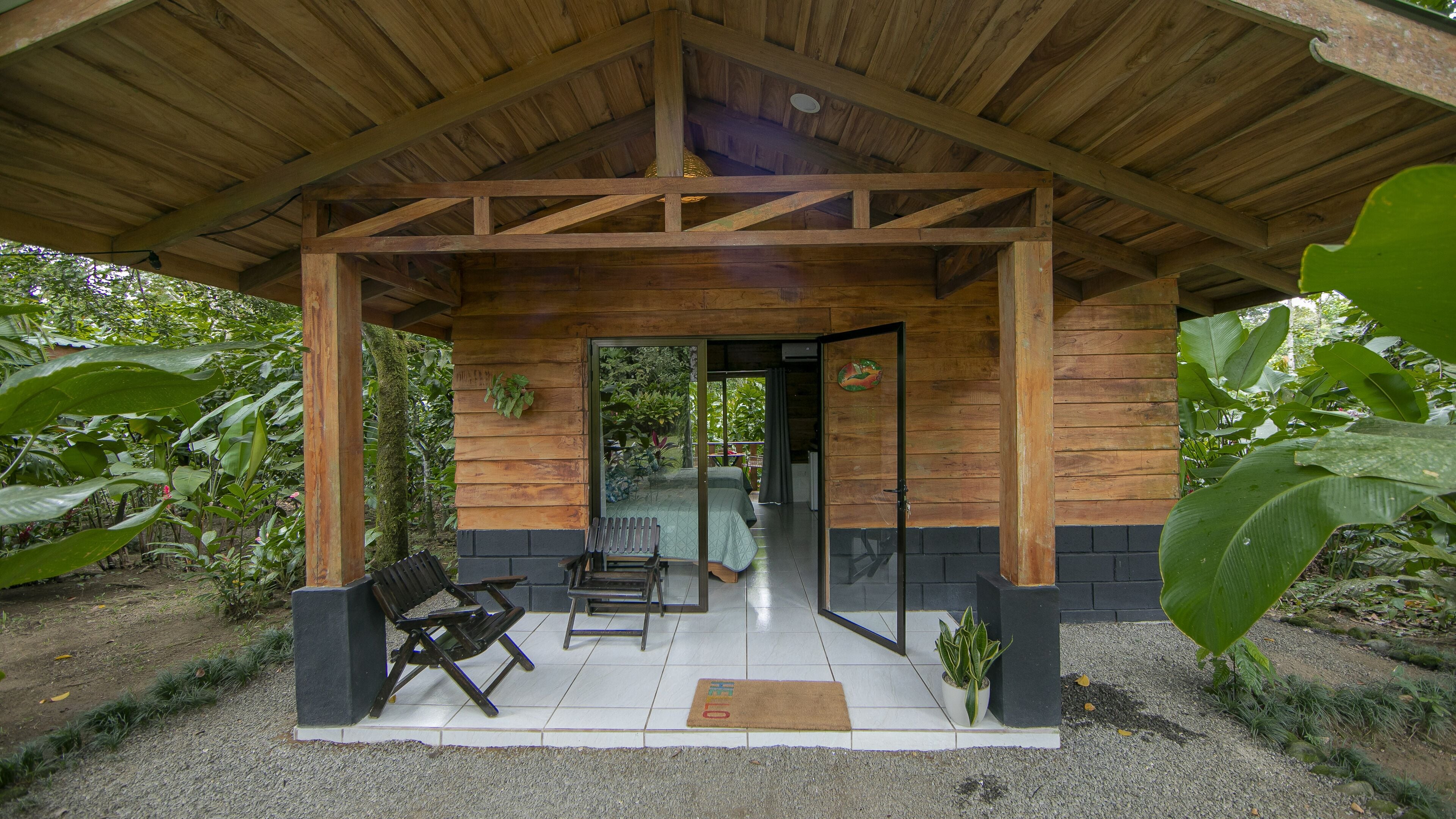 A wooden cabin with a covered porch, two benches, and a small potted plant.