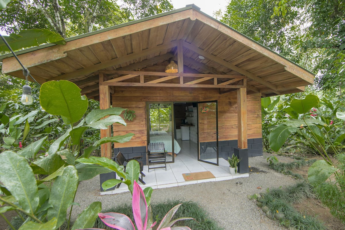 A wooden cabin with a glass door entrance, surrounded by lush greenery.