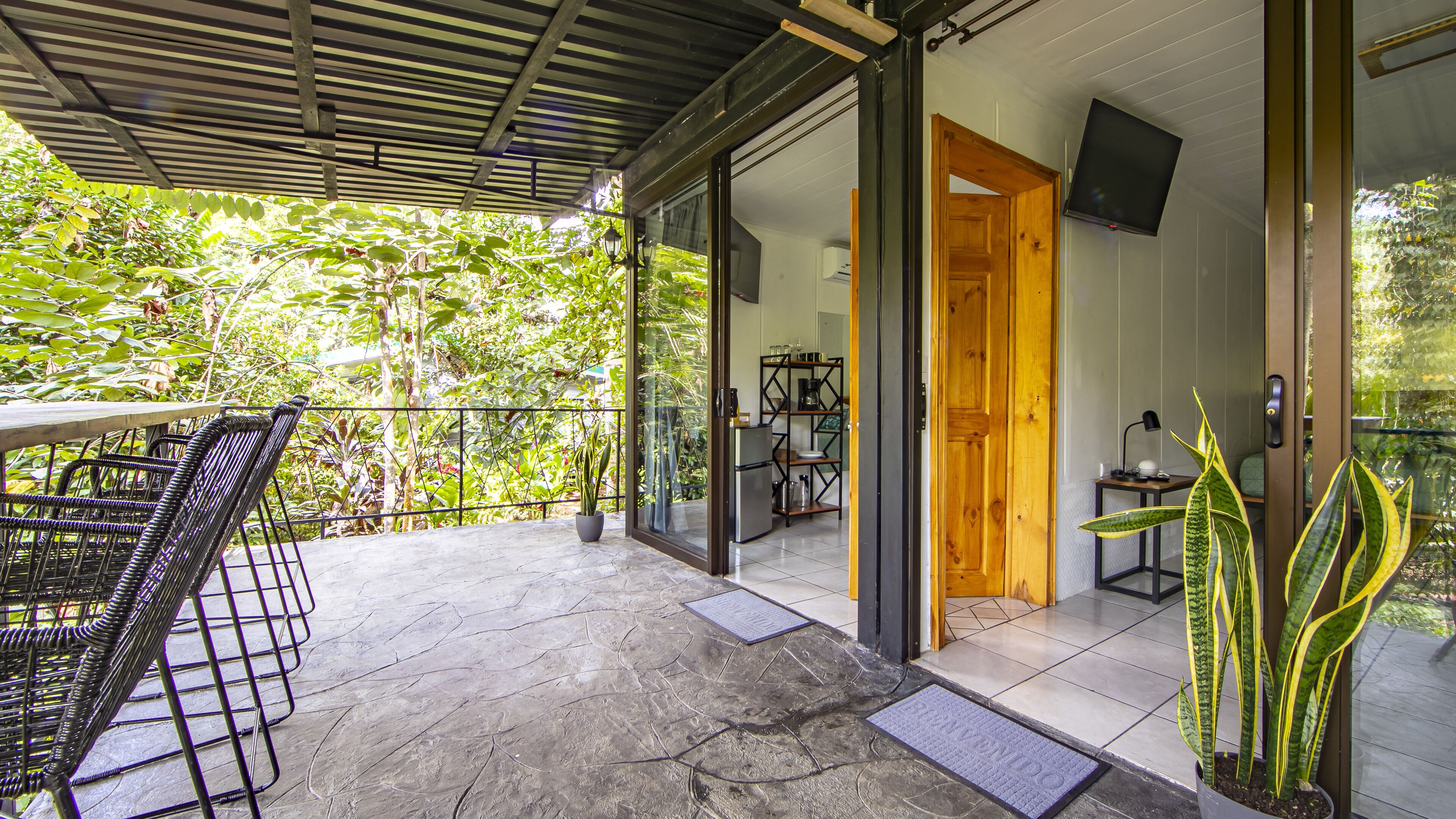 A covered patio with a table and chairs, a refrigerator, and a TV in a room with a wooden door.